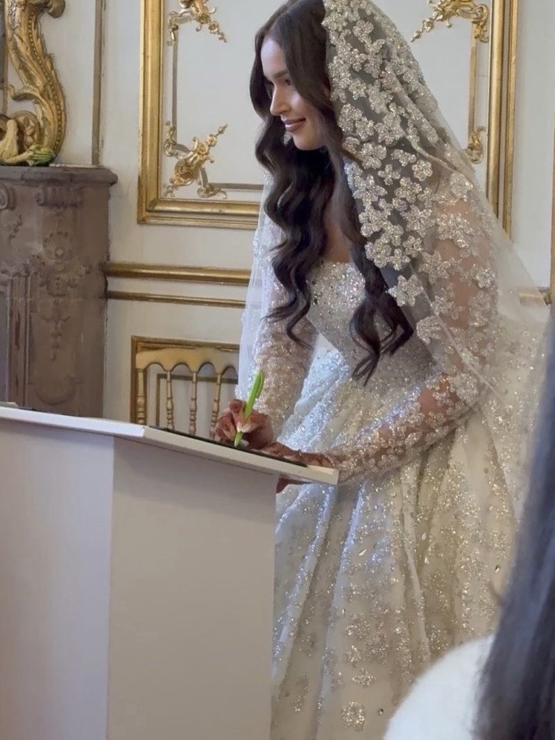 Mariee signant le registre a la mairie, voile de tulle brode de fleurs argentees et robe entierement perlee