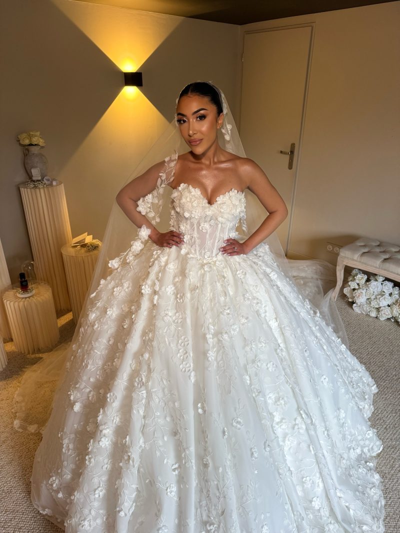 Mariee en robe princesse ivoire a bustier coeur et fleurs en relief, voile long, dans la piece des preparatifs